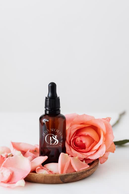 Dropper bottle with a monogram label beside a rose
